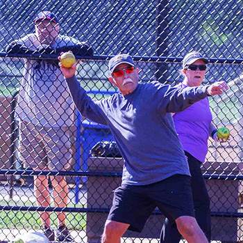 Man throwing softball with two people watching.